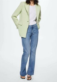 Jasnozielona teksturowana marynarka z postrzępionymi krawędziami, zestawiona z białym t-shirtem i niebieskimi dzwonowatymi dżinsami. Dopełnieniem stroju są czarne sandały z paskami.