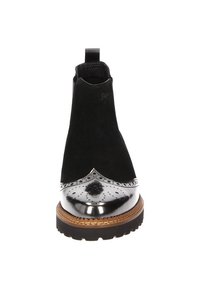Stivale alla caviglia in suede nero con punta metallica lucida, dettagli brogue e suola testurizzata. Dotato di un nastro per una facile calzata.