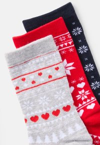 Ensemble de trois chaussettes : gris clair avec cœurs rouges et flocons de neige blancs, rouge vif avec motifs blancs, et bleu marine avec flocons de neige blancs.