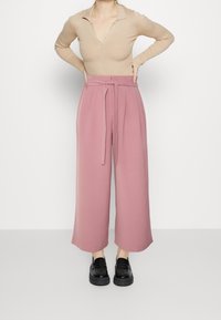 Rosa vida byxor med hög midja, framveck och ett matchande knytbälte. Sammanvävt med en beige ribbad långärmad topp.