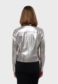 Veste argentée métallique au design ajusté, à manches longues et avec un col. Texture lisse avec des coutures visibles et une coupe courte.