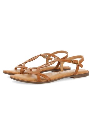 Par af brune flade sandaler med tynde læderstropper og lille guldlås, åben tå og slingback-stil på hvid baggrund.