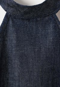 Tissu en denim bleu foncé formant la partie supérieure d’un vêtement sans manches avec un col rond et des coutures visibles.