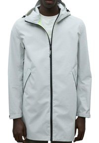 Chaqueta impermeable de color gris claro con capucha ajustada, cremallera negra, bolsillos laterales y tejido texturizado sutil. Diseño moderno y minimalista.