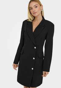 Abito blazer nero con maniche lunghe, due tasche frontali e bottoni decorativi argentati. Caratterizzato da scollatura a V profonda e design sartoriale.