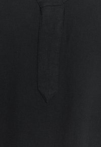Schwarzes Leinenoberteil mit scharfem Kragen und einer zentralen Knopfleiste. Die Textur ist leicht strukturiert und verleiht einen anspruchsvollen Look.