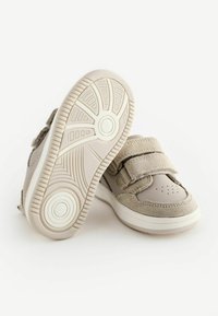 Beige Sneakers aus einer Kombination von glatten und strukturierten Materialien, mit Klettverschluss und einer Gummisohle mit strukturiertem Profil.