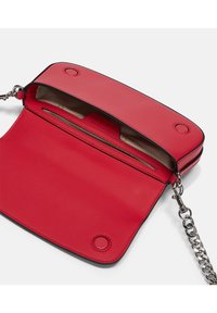 Czerwona skórzana torebka na ramię z teksturowaną powierzchnią, srebrnym łańcuszkiem, z górnym klapkiem i wewnętrznymi kieszonkami na karty. Otwarta, aby pokazać wnętrze.