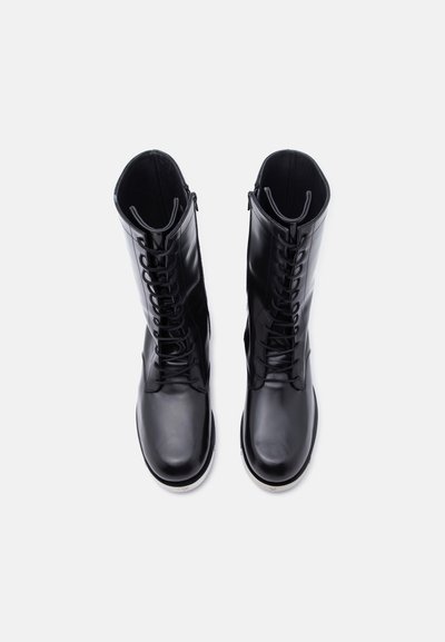 Ζευγάρι μαύρα, δερμάτινα αρβυλάκια με γυαλιστερή επιφάνεια και κορδόνια, που έχουν θέα από πάνω σε λευκό φόντο.