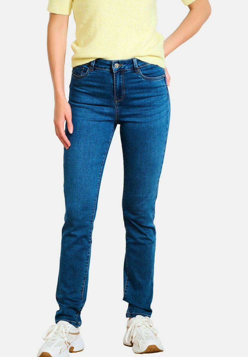 Niebieskie dżinsy o slim fit, z pięcioma kieszeniami i pojedynczym guzikiem na górze. Zestawione z jas żółtym swetrem i białymi trampkami.