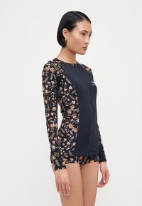 Long-sleeve swimsuit featuring a floral print in shades of orange and black, with a zip front and contrasting solid panels on the sides.