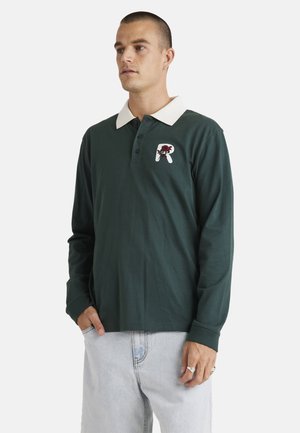 Green long-sleeve polo shirt with a white collar, featuring a floral logo patch on the chest and ribbed cuffs. Casual fit and soft fabric.