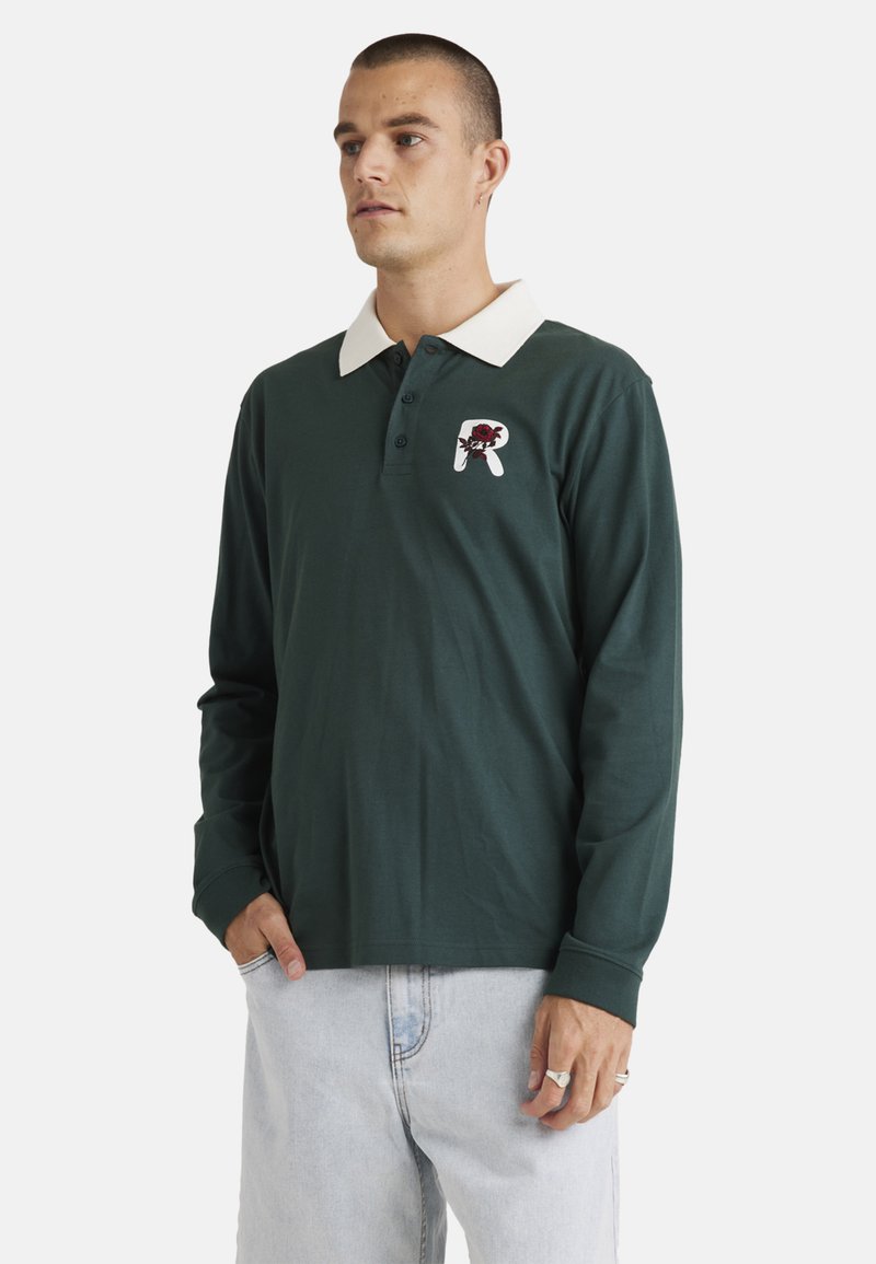 Green long-sleeve polo shirt with a white collar, featuring a floral logo patch on the chest and ribbed cuffs. Casual fit and soft fabric.