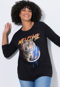Camisa de manga larga negra con un gráfico de tigre, que presenta un vibrante texto de "BIENVENIDO" y salpicaduras de color. Tejido suave y corte relajado.