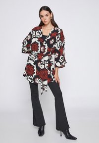 Blusa de flores en rojo, blanco y negro con cintura ajustada, mangas acampanadas y escote en V pronunciado, combinada con pantalones negros ajustados y botines.