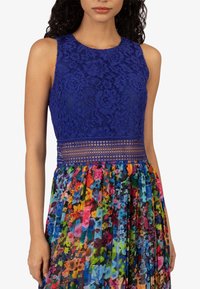 Blauwe kant mouwloze top met een bloemen geplooide multicolor rok; ingewikkeld bloemmotief met een gestructureerde tailleband en levendige kleuren.