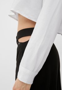 Witte cropped shirt met losse mouwen, in contrast met hoge zwarte broek met uitsnijding bij de taille en metalen label.