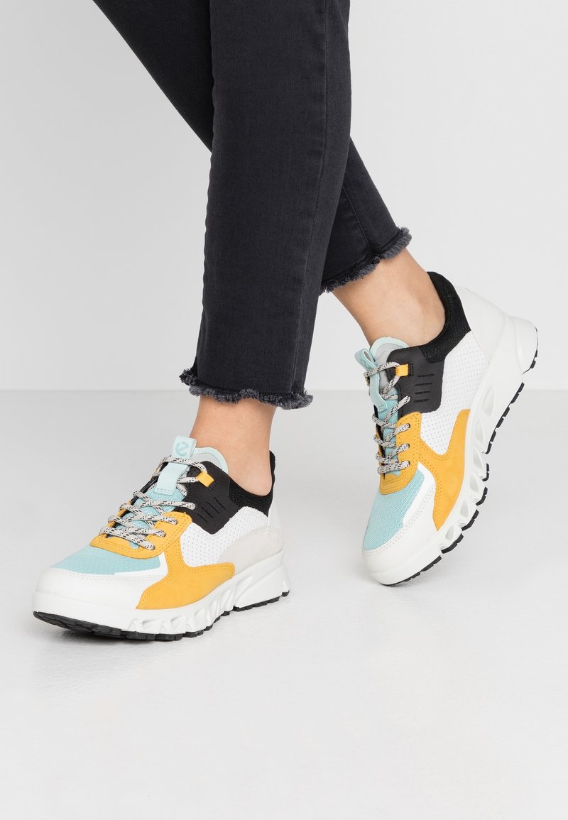 Färgglada sneakers med en blandning av svart, vitt, gult och ljusblått, med övre del i andningsbart nät, kraftig sula och texturerade snören.