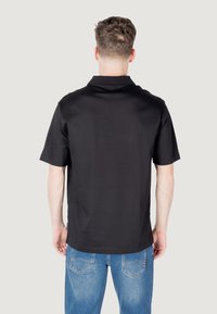 Polo shirt nera a maniche corte realizzata in tessuto liscio, con colletto classico e orlo dritto, indossata con jeans in denim blu.
