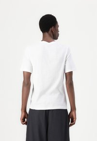 White cotton T-shirt with short sleeves and a round neckline, featuring a relaxed fit and smooth texture, viewed from the back.