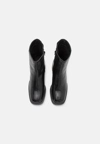 Black leather ankle boots with a smooth texture, square toe design, and side zippers. Feature minimalistic style and flat soles.