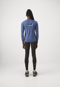 Long-sleeve blue shirt with "Patagonia" logo and mountain design on back, paired with black leggings and athletic shoes.