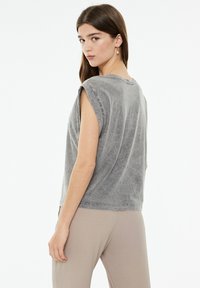 Camiseta gris de gran tamaño con bordes deshilachados y mangas cortas, que presenta un corte holgado y una textura suave. Llevada con pantalones de color claro.