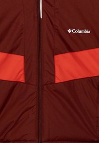 Bordó dzseki piros kiegészítőkkel és középső cipzárral. Simára és könnyű anyagból készült, a Columbia logó a felső sarokban található.