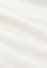 Gros plan d'un tissu côtelé blanc montrant ses lignes parallèles texturées et sa surface douce.