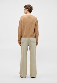 Καφέ πλεκτό πουλόβερ με χαλαρή εφαρμογή σε συνδυασμό με ανοιχτό μπεζ παντελόνι με φαρδιά γραμμή. Το παντελόνι διαθέτει πίσω τσέπες και λεπτή υφή.