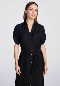 Czarna sukienka zapinana na guziki, wykonana z miękkiego materiału, z krótkimi rękawami, paskiem do związania w talii i guzikami w złotym odcieniu z przodu.