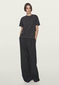T-shirt nera in cotone con maniche corte e collo rotondo, abbinata a pantaloni neri larghi, caratterizzati da pieghe nette e una texture liscia.