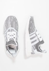 Svartvita mönstrade träningsskor med stickad ovandel, med en vit mellersta sula och grå detaljer vid hälen och tungan.