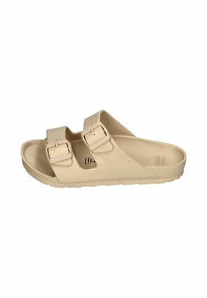 Two beige buckle sandals floating on clear blue swimming pool water with light reflections and water droplets on sandals.