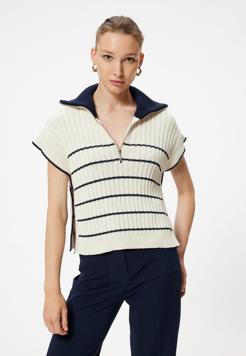 Stickad tröja med dragkedja, i krämfärgad med marinblå ränder, korta ärmar och ståkrage. Texturerad, ribbad material.