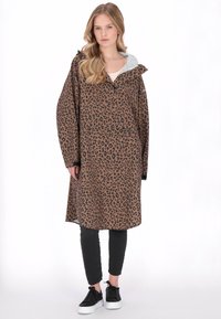 Barna leopárdmintás kabát kapucnival, elülső zsebbel és hosszú ujjakkal. Fekete nadrág és fekete tornacipő fölött viselve.