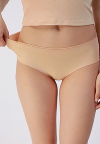 Kerge beež seamless aluspüks, millel on sile tekstuur, elastne vöökoht ja kerge läige, tõmmatakse üles, näidates lähedast istuvust.