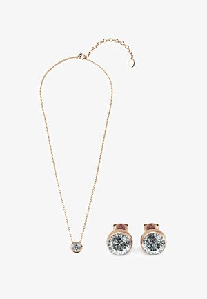 Set di gioielli in tonalità oro composto da una delicata collana con un pendente rotondo e orecchini a bottone coordinati, entrambi impreziositi da gemme trasparenti e rotonde.