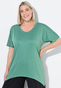 T-shirt vert à manches courtes fabriqué à partir d'un matériau texturé et léger. Il présente un col rond et une longueur de dos arrondie et plus longue.
