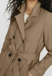 Lichtbruin trenchcoat met een dubbelknopssluiting, grote kraag, ceintuur in de taille en zwarte knopen; gladde stof met een getailleerde pasvorm.