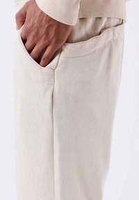 Beige katoenen broek met een zijzak. De stof lijkt zacht en glad, met een relaxte pasvorm en een elastische tailleband.
