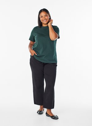 Donkergroen t-shirt met korte mouwen, relaxed fit, gecombineerd met zwarte wijde broek. Zwarte balletschoenen met decoratieve accenten.