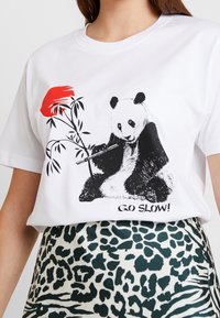 Vit bomulls t-shirt med en svartvit pandaillustration som håller i bambu och en röd blomma, med texten "KÖR LUGNT!" nedanför.