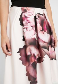 Blommig veckad kjol i krämfärgad tyg med stora, abstrakta rosa och svarta blommönster, med en slät textur och en skarp form.