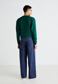 Green long-sleeve shirt paired with wide-leg blue pinstriped jeans, featuring two back pockets and a relaxed fit.
