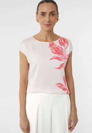 Short-sleeve pink blouse with red leaf print, smooth texture, round neckline, and relaxed fit. Paired with white high-waisted trousers.