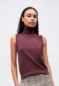 Lila ilmanhiha turtleneck-toppi, jossa on sileä neulospinta ja ribbivaatteet, suora helma, yhdistettynä ruudullisiin korkeavyötäröisiin housuihin.