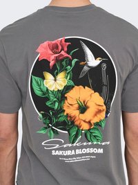 Rückseite eines T-Shirts mit buntem Blumendesign, gelbem Schmetterling, weißem Kolibri und dem Schriftzug "Sakura Blossom" auf grauem Stoff.