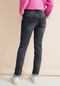Jeans de mezclilla gris con un corte slim, que presentan dos bolsillos traseros, un ligero desgaste y dobladillos enrollados, combinados con zapatillas blancas.