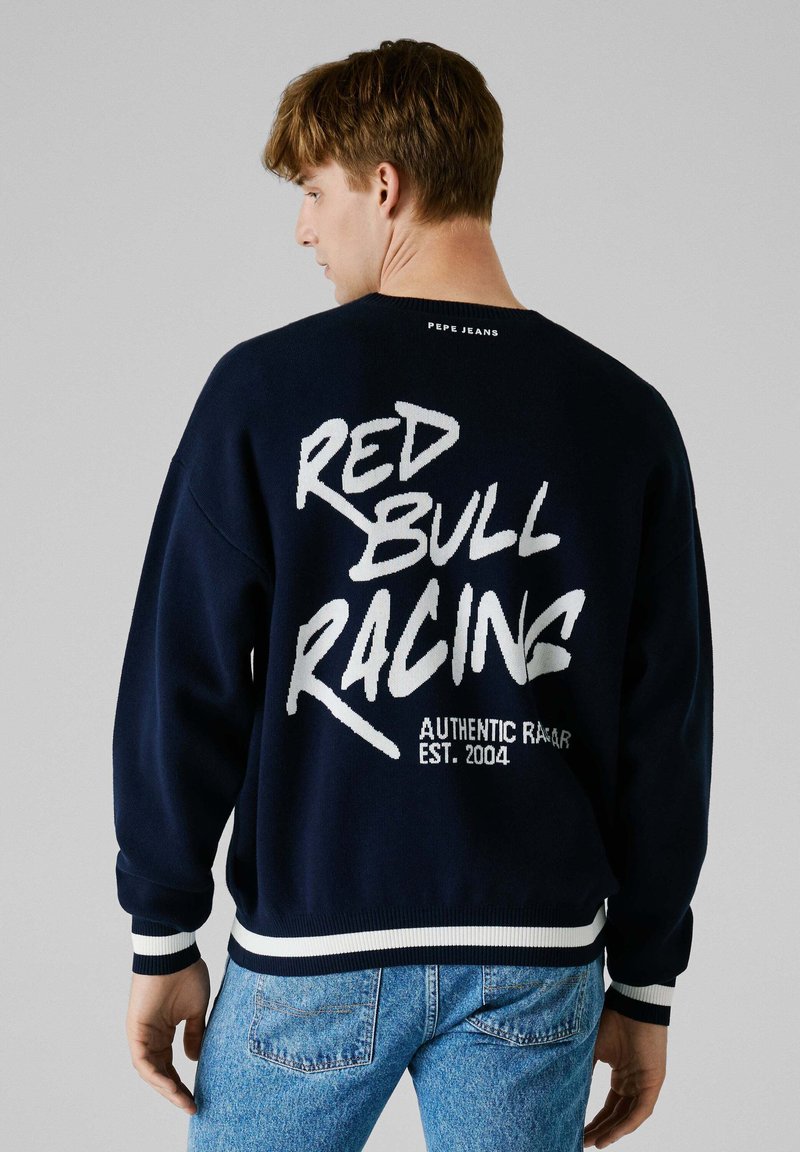 Granatowa bluza z dużym białym nadrukiem "RED BULL RACING" z tyłu, z kontrastowymi białymi i granatowymi ściągaczami przy mankietach i dole.